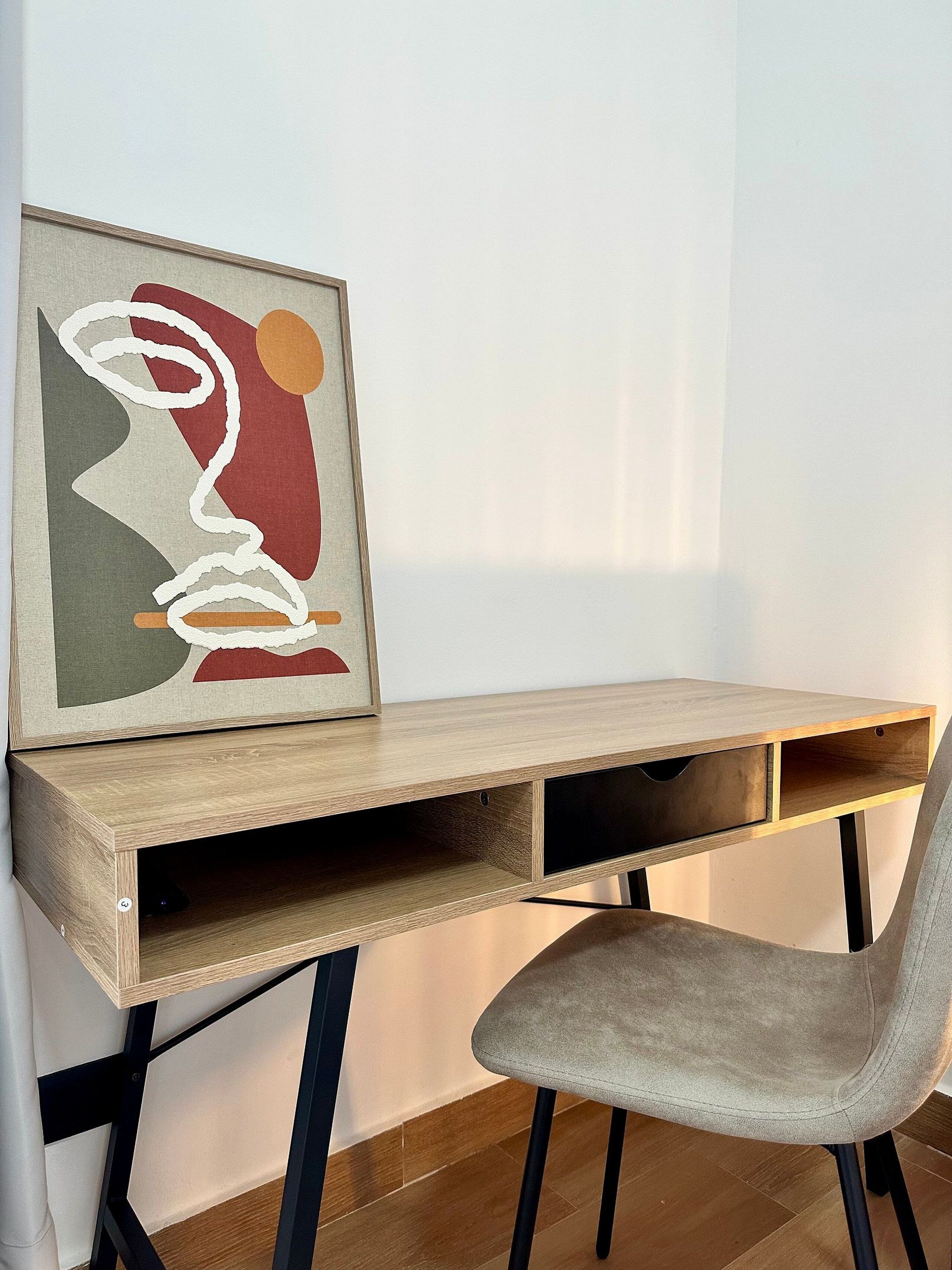Een houten bureau met een comfortabele stoel, een lijst met abstract schilderij en een effen muur.
