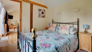A bedroom with a bed, wooden headboard, floral bedspread, bedside lamps, and a wooden nightstand. - 1 Bed in Banningham (oc-1389) (Banningham)