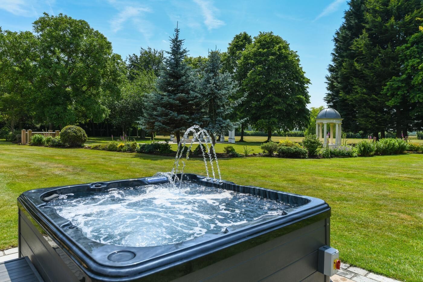 Un jacuzzi en un jardín con un quiosco al fondo.