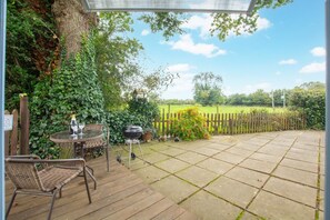 A patio with a table and chairs, a barbecue grill, and a view of a green field. - 1 Bed in Banningham (oc-564) (Banningham)