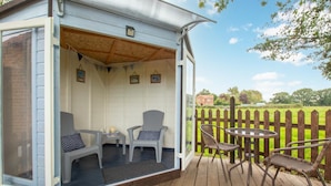 A covered outdoor seating area with two chairs and a table, a wooden deck, and a view of a green field and a wooden fence. - 1 Bed in Banningham (oc-564) (Banningham)
