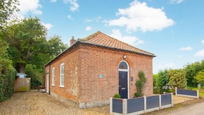 A small brick building with a tiled roof, a dark door, and a small garden area with a fence. - 1 Bed in Banningham (oc-564) (Banningham)