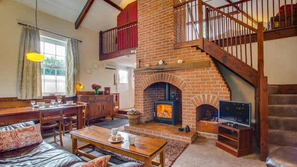 A cozy living room with a fireplace, a wooden staircase, and a dining area with a bench and table. - 1 Bed in Banningham (oc-564) (Banningham)