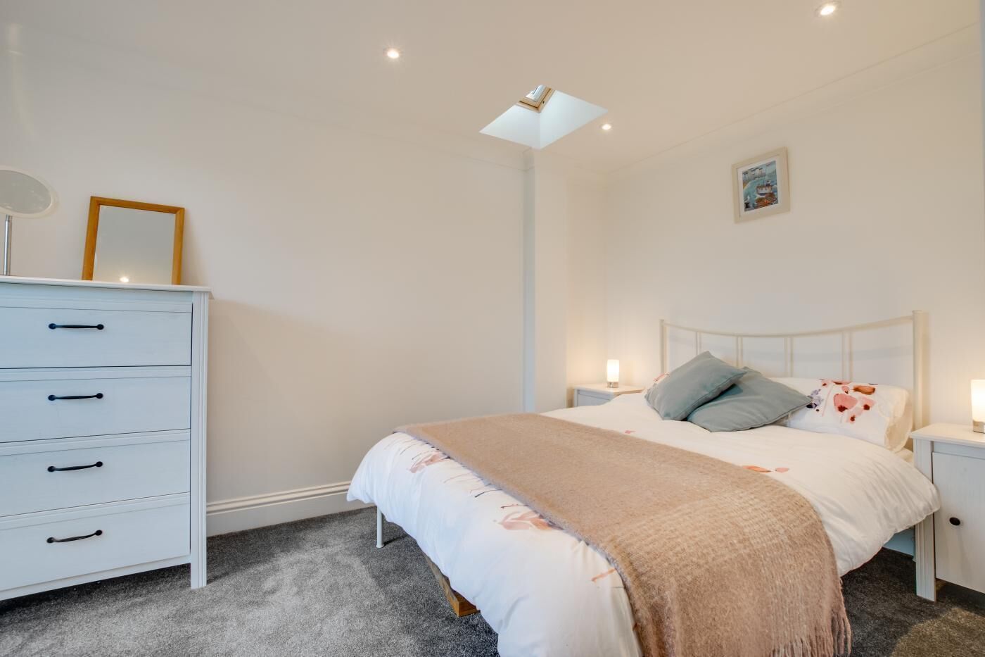 Un dormitorio con cama, mesitas de noche, cómoda y luz en el techo.