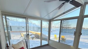 Quarto com cama, ventoinha no teto e janelas amplas com vista para um deck coberto de neve e um lago.