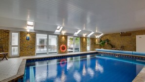En indendørs swimmingpool med flisekant, murstensvæg og et loft med ovenlys.