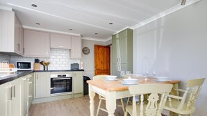 A modern kitchen with light-colored cabinets, a wooden dining table set with white plates and glasses, and a built-in oven. - 2 Bed in Holt (oc-1449) (Holt)