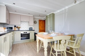 A modern kitchen with light-colored cabinets, a wooden dining table set with white plates and glasses, and a built-in oven. - 2 Bed in Holt (oc-1449) (Holt)