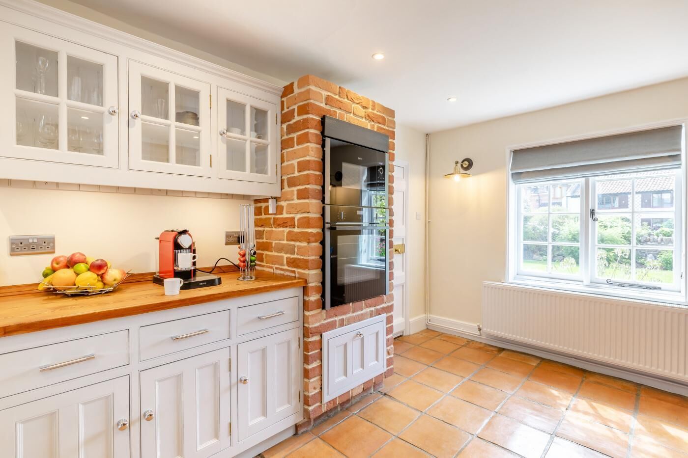 A kitchen with white cabinets, a brick oven, and a window with a view of greenery.