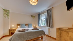 Un dormitorio con una cama de madera, una mesita de noche con lámpara, una ventana con cortinas y un televisor fijado a la pared.