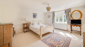 Une chambre à coucher comprenant un lit, des tables de chevet, une commode, un téléviseur et une fenêtre avec des rideaux.
