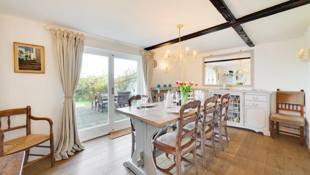 Un coin repas avec une table et des chaises en bois, une cuisine avec des placards blancs et une grande fenêtre avec des rideaux.