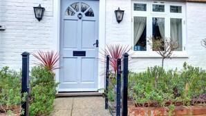Une maison en briques blanches avec une porte bleue, des lanternes noires et une fenêtre avec des rideaux.