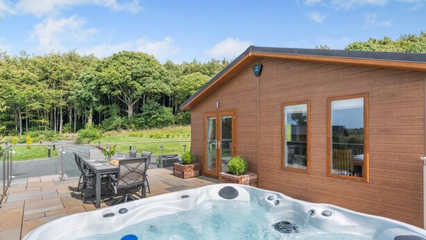 A wooden cabin with a hot tub, patio furniture, and a view of a forested area.