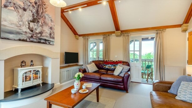 Een ruime woonkamer met een open haard, een leren bank, een bijzettafeltje en een schilderij van paarden.