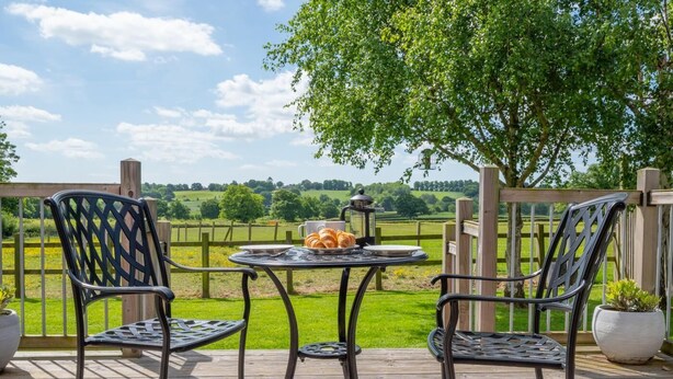 Um terraço com duas cadeiras e uma mesa, com vista para uma paisagem verde.