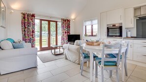 Uma sala de estar moderna com um sofá branco, uma mesa de jantar com cadeiras, uma televisão e uma área de cozinha com armários e fogão.