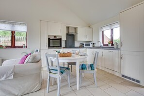 A compact kitchen with white cabinets, a dining table, and chairs. - 1 Bed in Rolvenden (oc-tn612) (Rolvenden)
