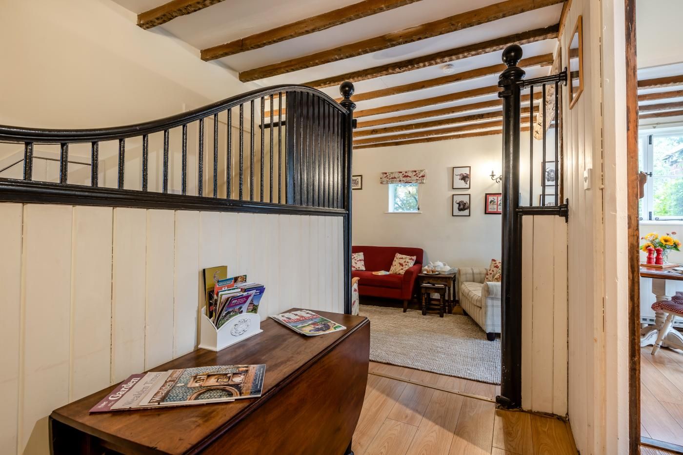 Un escalier en bois avec une balustrade noire mène à un salon où se trouvent un canapé rouge, une petite table et un tapis à motifs.