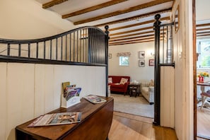 Una escalera de madera con barandilla negra que conduce a una sala de estar con un sofá rojo, una mesita y una alfombra estampada.