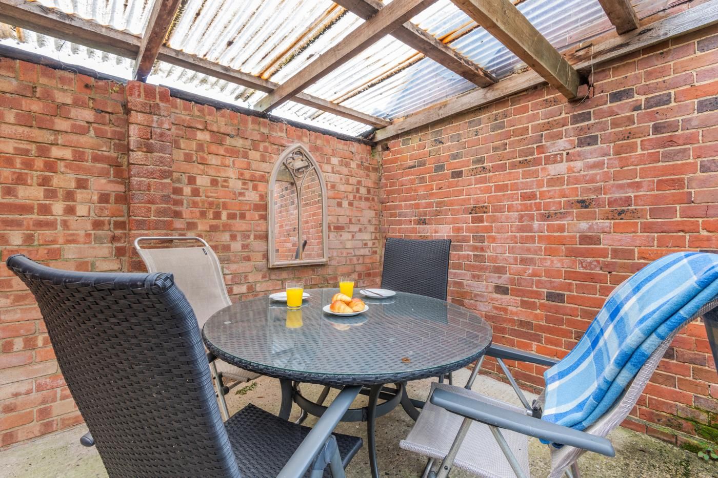 A brick patio with a round table and chairs, a glass enclosure, and a decorative mirror.