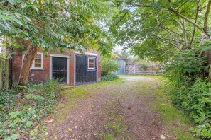 A brick building with a black gate, surrounded by dense foliage and a gravel path. - 2 Bed in Rolvenden (oc-tn563) (Rolvenden)