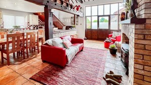 A spacious living area with a red sofa, a fireplace, and a kitchen in the background. - 3 Bed in Holt (oc-1331) (Bodham)