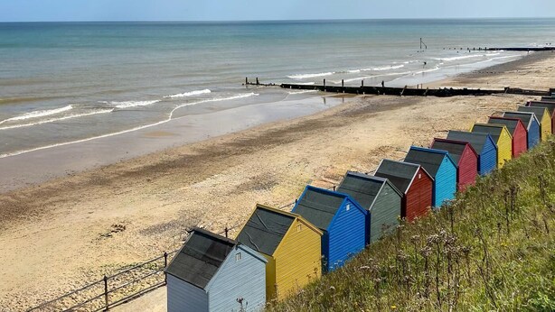 A beach with a row of colorful beach huts along the shore. - 3 Bed in Holt (oc-1331) (Bodham)