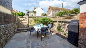 A patio with a table and chairs, a barbecue grill, and a stone wall. - 4 Bed in Rottingdean (oc-bbrott) (Brighton)