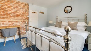 A bedroom with a metal-framed bed, a brick wall, a small table, and a mirror on the wall. - 4 Bed in Rottingdean (oc-bbrott) (Brighton)