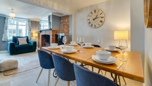 A dining area with a wooden table set for four, a brick fireplace, and a large wall clock. - 4 Bed in Rottingdean (oc-bbrott) (Brighton)