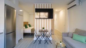 A compact living space with a kitchenette, a dining area with a table and chairs, a sofa, and a TV mounted on the wall. - Golden Sunrise By CanariasGetaway (Mogán)