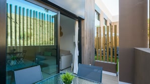 A modern outdoor patio with a glass table and chairs, a potted plant, and a view of a wooden fence and greenery. - Golden Sunrise By CanariasGetaway (Mogán)