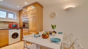 Una cucina moderna con mobili in legno, forno integrato, microonde e lavatrice. C'è un tavolo da pranzo con sedie e un orologio sulla parete.