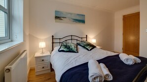 Una camera da letto con un letto, due comodini con lampade, un termosifone, un quadro appeso al muro e una porta in legno.