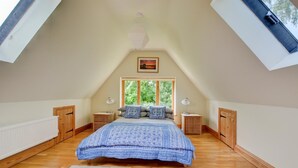 Een slaapkamer met schuine wand, een groot bed, twee nachtkastjes, een raam met uitzicht op bomen en een plafondlamp.