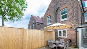 Een terras met houten omheining, een tafel met stoelen en een bakstenen gebouw op de achtergrond.