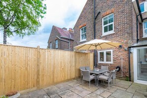 A patio with a wooden fence, a table with chairs, and a brick building in the background. - 4 Bed in Rye (oc-rh1168) (Rye)