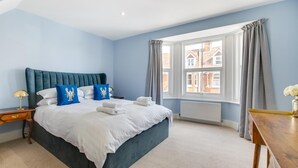 Een hotelkamer met een groot bed, een nachtkastje, een houten bijzettafeltje en een raam met gordijnen.