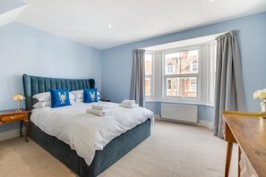 A hotel room with a large bed, a nightstand, a wooden side table, and a window with curtains. - 4 Bed in Rye (oc-rh1168) (Rye)