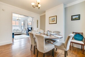 A dining area with a round table set for six, surrounded by six chairs. There is a chandelier above the table, and a fireplace is visible in the background. - 4 Bed in Rye (oc-rh1168) (Rye)