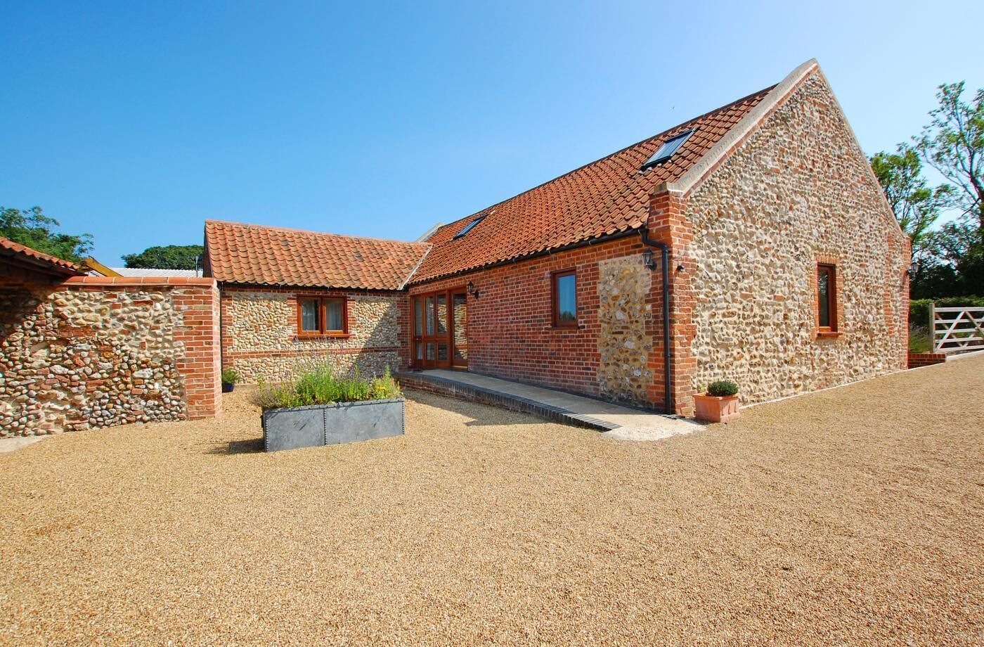 A stone and brick building with a tiled roof, a gravel driveway, and a small garden area.