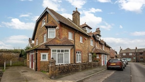 A two-story brick house with a tiled roof, a front garden, and a parked car on the street.