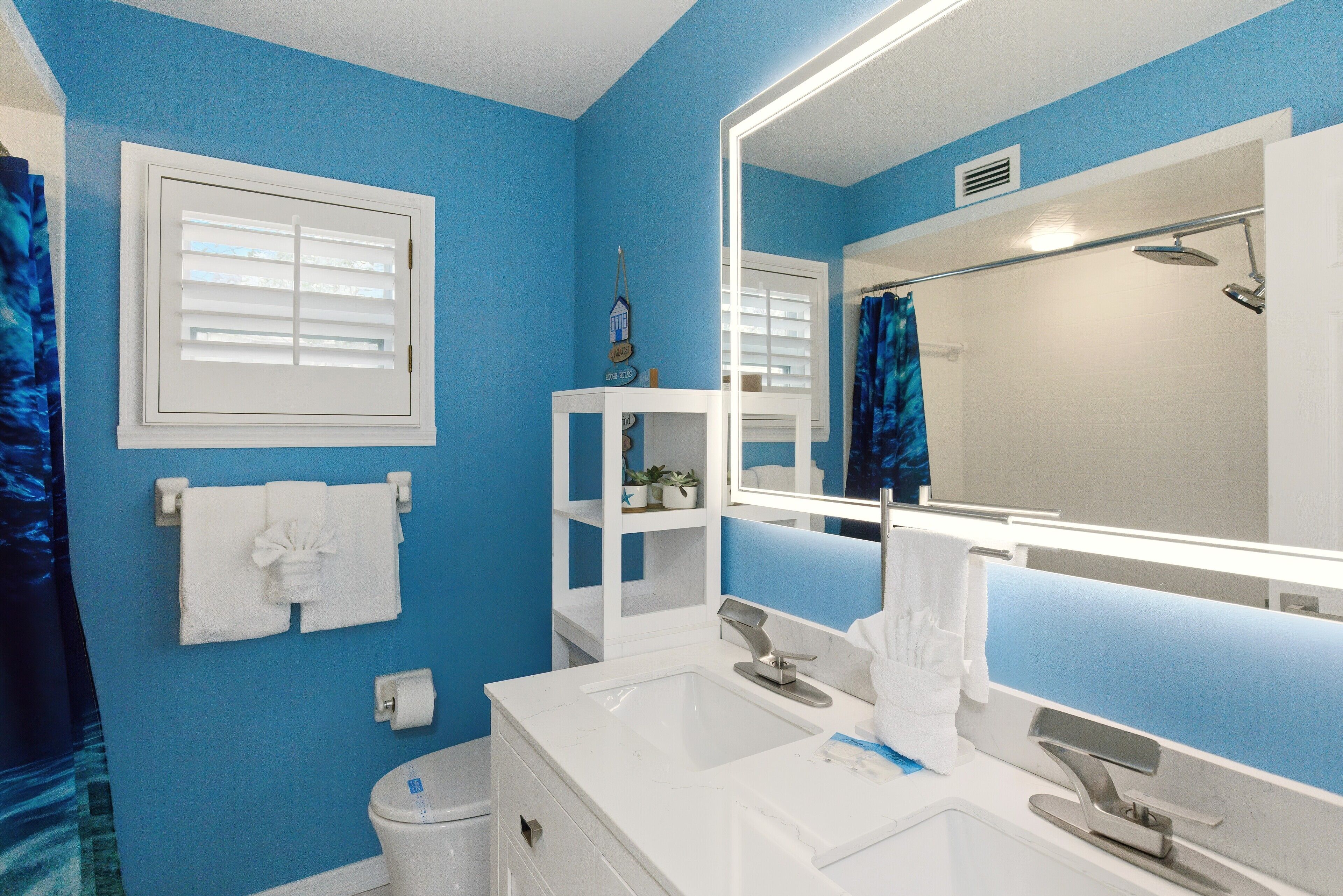 A bathroom with blue walls, a white sink, a mirror, and a shower.