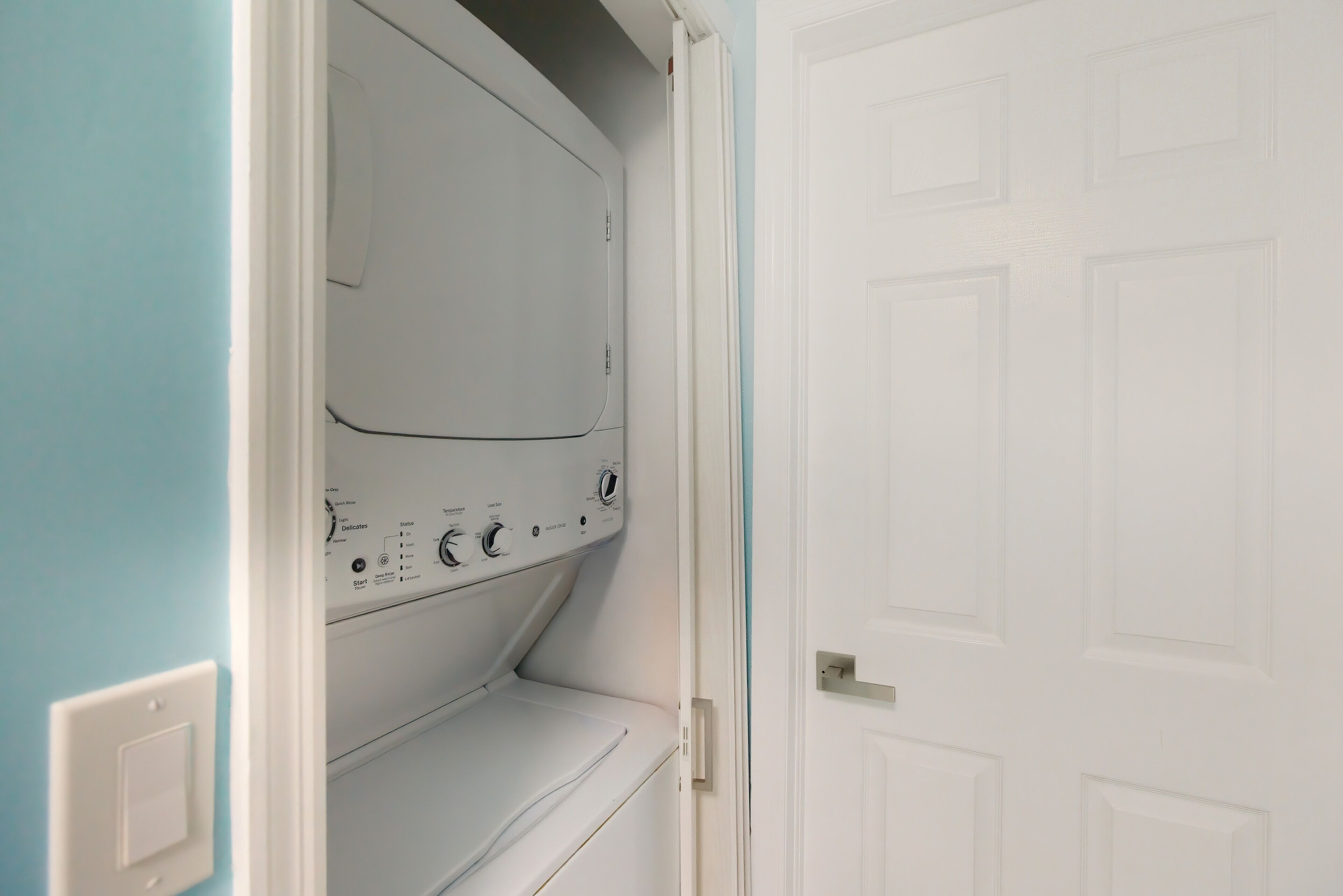 A laundry room with a washing machine and dryer, a white door, and a light switch on the wall.