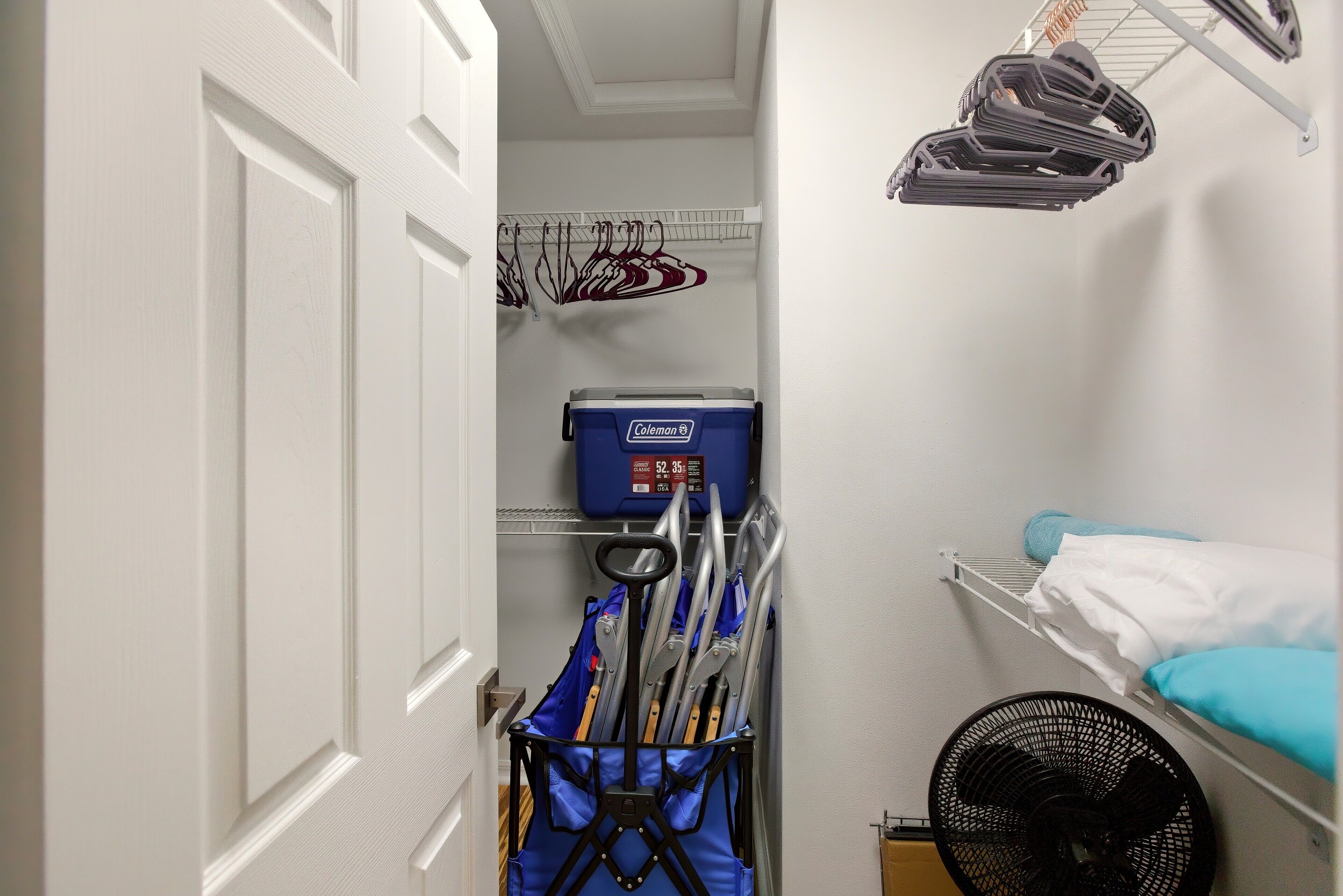 A narrow hallway with a storage closet, a fan, and hanging clothes racks.