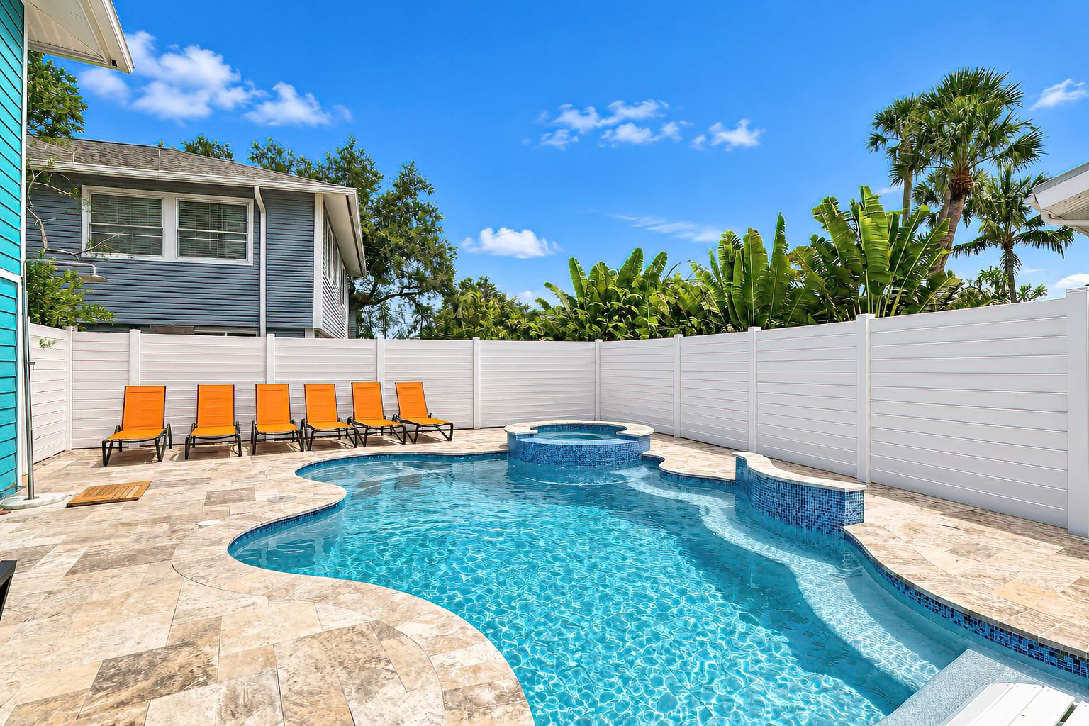 A swimming pool with a curved design, surrounded by a white fence, and featuring orange lounge chairs.