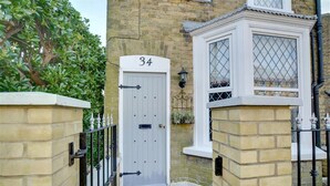 A traditional brick house with a white door marked with the number 34, a small window with a lattice design, and a black metal gate. - 3 Bed in Broadstairs (oc-th006) (Broadstairs)