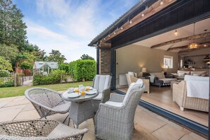 A patio with wicker furniture and a glass door leading to an interior living area with sofas and a dining table. - 3 Bed in Sedlescombe (oc-c32764) (Sedlescombe)