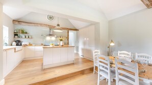 A modern kitchen with white cabinets, a wooden island, and a dining area with white chairs and a wooden table. - 3 Bed in Sedlescombe (oc-c32764) (Sedlescombe)